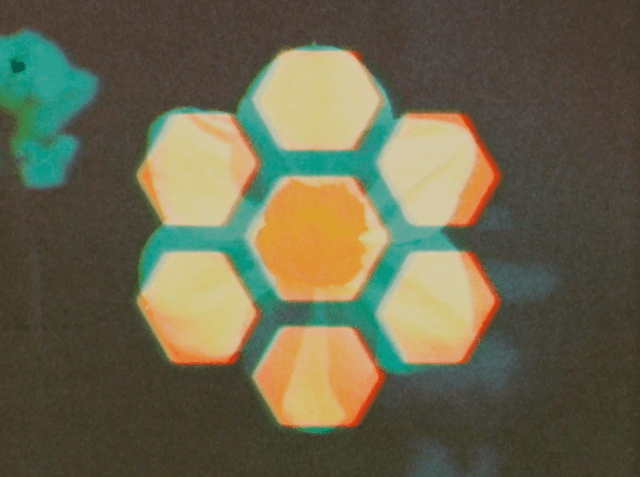 A blurry, glowing hexagonal symbol in teal and orange, echoing the haunted analogue mood of Boards of Canada and Inferno.